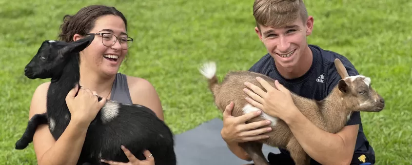 A couple of people sitting on a yoga mat holding goats